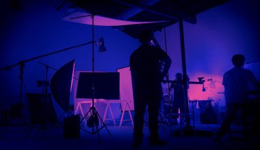 Neon mavisi pembe renkli çekim. Büyük stüdyoda kurulmuş video prodüksiyon sahnesinin arkasında. Ekip çalışıyor ve kamera ekipmanları siluette. Film yapım endüstrisi. Işıklandırma ayarlandı.