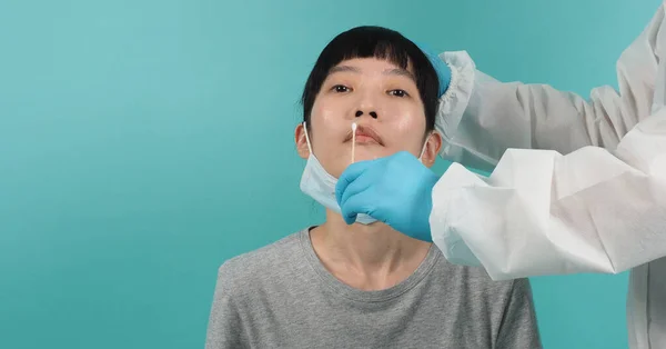 Covid 19 swab test. woman with PCR test. Coronavirus test during epidemic. Medic taking sample for virus testing. studio shot and blue green background. Doctor in PPE suit swab testing.