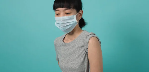 Vaccine Concept. Woman waiting for coronavirus vaccine injection by doctor. Asian woman with medical mask open shoulder and upper arm on blue green background. Waiting for vaccination.