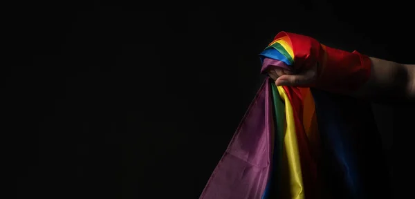 LGBTQ pride flag. Lesbian Gay Bi sexsual Transgender Queer. Homosexsual pride Rainbow flag in gay hand. black background. Represent symbol of freedom, peace, equality and love. LGBTQ concept.