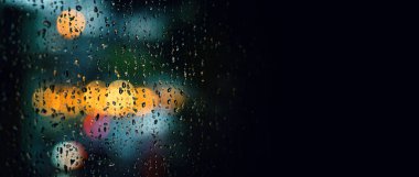 Geceleri pencereye yağmur damlası düşer. Bangkok Tayland 'da yağmurlu bir mevsimde apartman dairesi ya da apartman penceresi. Pencerenin dışı bulanık. Şehir ışığı, doğal ağaç ve gökyüzü..  