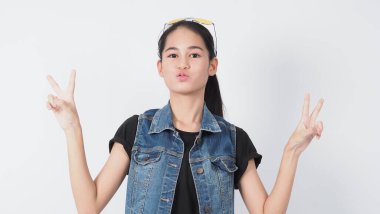 Beyaz arka planda duran Asyalı genç kadın hareketi. Neşeli ve kendinden emin. Mini kalp gibi mimimikler gösteriyor Tamam başparmak yukarı ya da işaret. Mutlu, heyecanlı ve şaşırmış ceket kotları.