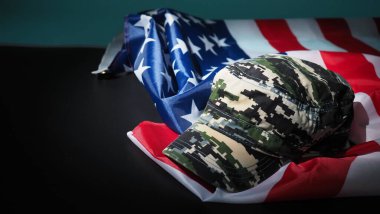Amerikan bayrağı ve askeri şapka veya çanta. Üst açı. Siyah arka planda Amerikan bayrağı olan asker şapkası ya da miğferi. Askeri konsepti kamuflaj objesi ve ABD bayrağı ile temsil et. 