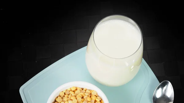 Soy milk with no sugar added in a glass on a green color plastic plate mat. Close-up images of home made healthy soy milk drink and soy beans in small bowl. Black background in a studio shot. Soymilk.