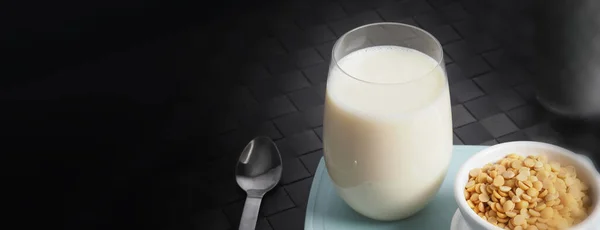 Soy milk with no sugar added in a glass on a green color plastic plate mat. Close-up images of home made healthy soy milk drink and soy beans in small bowl. Black background in a studio shot. Soymilk.