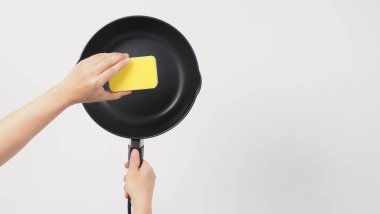 Tencere temizliği. Erkek adam beyaz arka planda, bulaşık deterjanıyla tencereyi temizlerken yumuşak tarafı sarı, yemek pişirdikten sonra hijyen için sert tarafı yeşil. Elektrik tavası. 