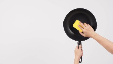 Tencere temizliği. Erkek adam beyaz arka planda, bulaşık deterjanıyla tencereyi temizlerken yumuşak tarafı sarı, yemek pişirdikten sonra hijyen için sert tarafı yeşil. Elektrik tavası. 