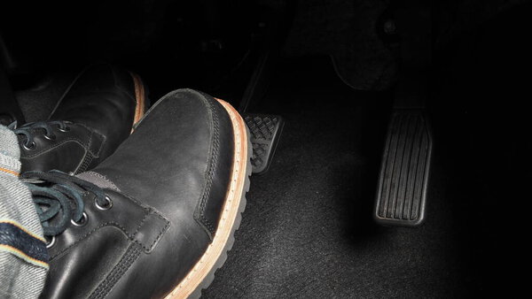 Man foot and accelerator and brake pedal inside the car or vehicle and copy space which black color leather shoe stepped on it for speed up or control automobile pace power. Automobile Driving concept