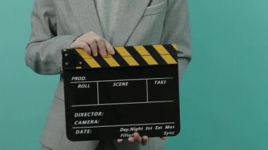 Film tahtası ya da alkış tahtası vuruşu. İş kadını elinde boş bir film tahtası tutuyor ve alkışlıyor. Sarı ve siyah alkışlar mavi yeşil arka planda izole edilmiş. video film üretimi.