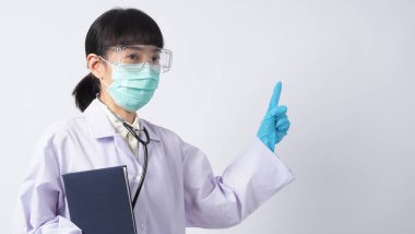 Üniformalı doktor boş bir bölgeyi işaret ediyor. Salgın virüsünü önlemek için mavi lateks eldivenler, temiz gözlükler ve yeşil N95 maskesi takıyor. Asyalı doktor. El hareketi. Tıbbi steteskop. Virüs Kitabı