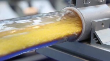 Plastik topaklar hava tüpleri. Otomatik makinede sarı plastik topaklar taşıyan saydam endüstriyel tüpü kapatın. Yüksek hızda hareket eden mühendislik materyali. Plastik üretim teknolojisi