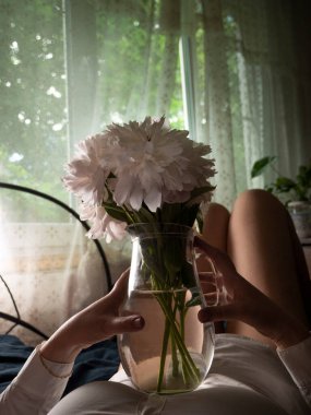 Beyaz elbiseli bir kızın siluetinde vazoda şakayık demeti