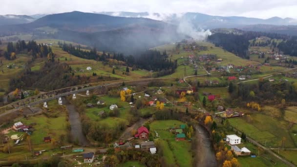 Вид с воздушного дрона на красочные осенние Карпатские горы. Горные массивы покрыты хвойными и смешанными лесами в ярких осенних цветах. Ниже вы можете увидеть деревенские дома. — стоковое видео