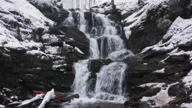 Dağlarda kış şelalesi. Su kar ve buzu delip geçer.