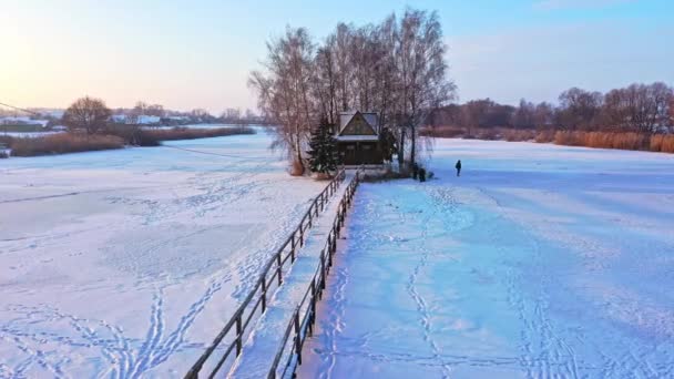 Vue aérienne d'une petite maison sur l'île. Paysage hivernal avec un pont vers la maison sur le lac. — Video