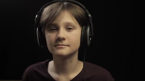 Tiener luisteren muziek in koptelefoon en dansen over donkere studio achtergrond — Stockvideo