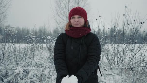 Kvinnan i en röd varm hatt kastar snö i vinterskogen. Aktiv livsstil, vinteraktivitet, utomhus vinterspel koncept. Julhelger. Långsamma rörelser — Stockvideo