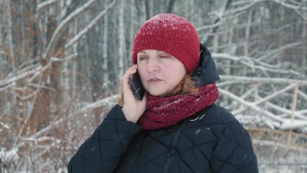 Mujer hablando por teléfono en el bosque de invierno en día nublado nevado en cámara lenta — Vídeo de stock