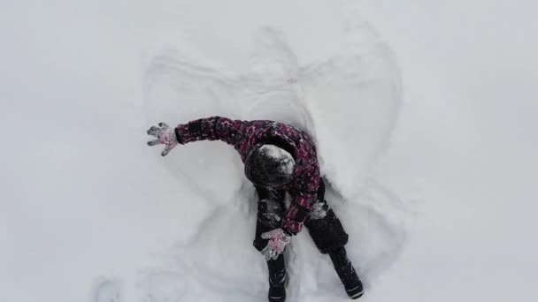 雪の地面に横たわって天使の姿、楽しい子供時代の概念を作る子供の男の子のトップビュー — ストック動画