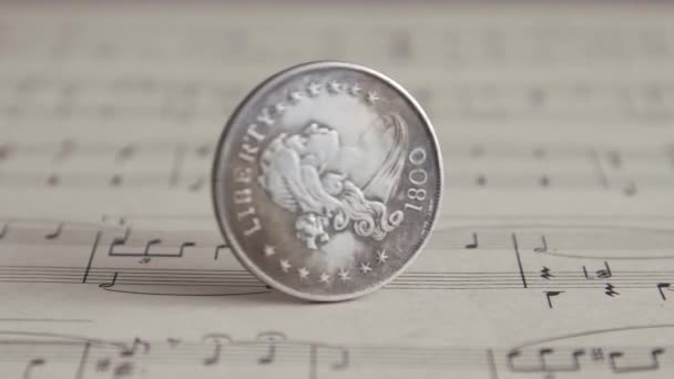 "Silver Old Coin Rotating On the Sheet of Music Close Up". Крутящаяся монета американских долларов. Оплата за творческую работу — стоковое видео