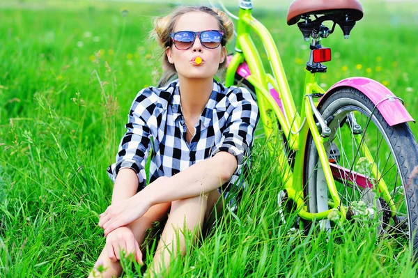 Dość młoda dziewczyna siedzi obok roweru w trawie — Zdjęcie stockowe