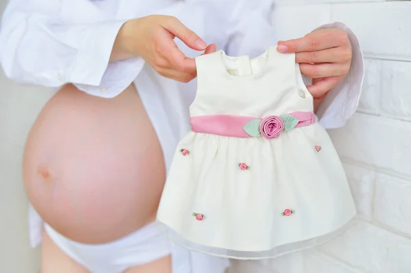 妊娠中の女性は赤ちゃんのドレスを保持 — ストック写真