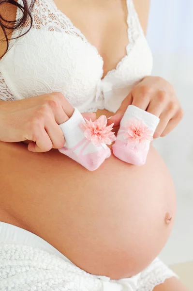 Mujer embarazada vientre y zapatos de bebé — Foto de Stock