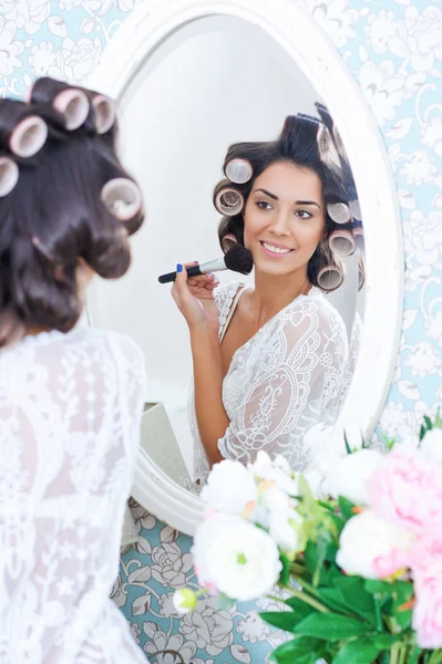 Beautiful woman in hair curlers puts on morning makeup