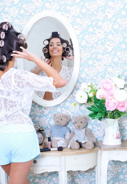 Женщина позирует перед зеркалом в бигуди для волос — стоковое фото