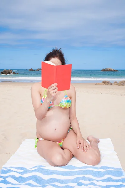 Bikini gravid läsa boken på stranden — Stockfoto