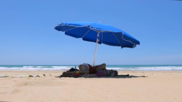 Baby und Mutter legen blauen Sonnenschirm am Strand nieder — Stockvideo