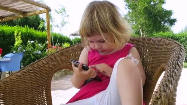 Baby sitzt im Weidenstuhl und telefoniert mit Handy — Stockvideo