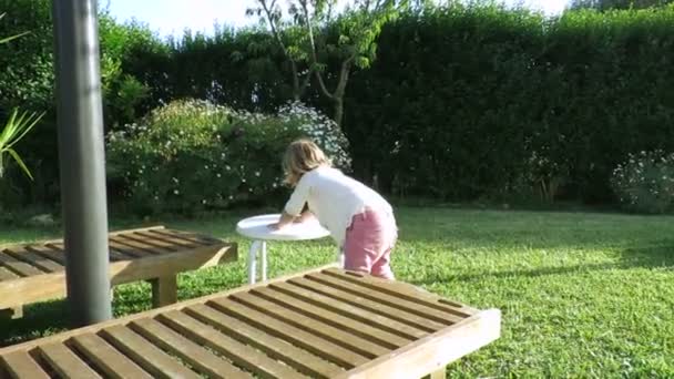 Baby dwa lata noszenia biały stół w ogrodzie — Wideo stockowe