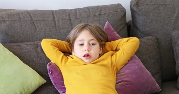 6歳の子供は快適な茶色のソファの上に横たわる彼女の手に彼女の頭を休める — ストック動画
