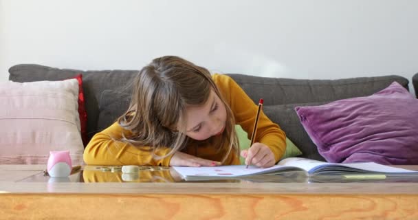 6歳の少女が茶色いソファに座り運動学校の本に宿題を書いて話をしていました — ストック動画