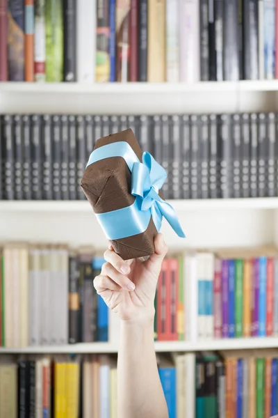 Mano con caja de regalo marrón sobre biblioteca —  Fotos de Stock