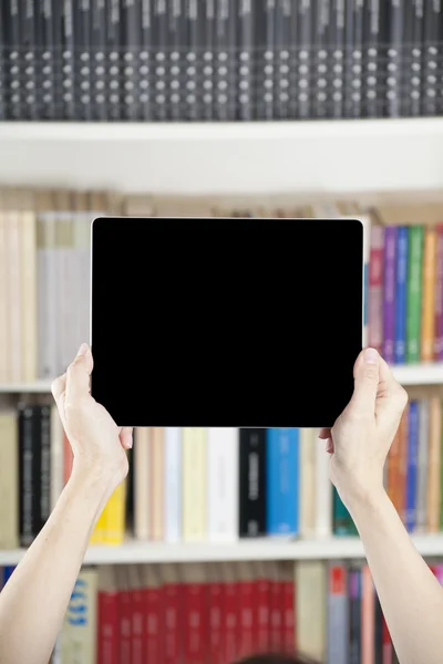 Τα χέρια που δείχνει την κενή οθόνη tablet πέρα από βιβλιοθήκη — Φωτογραφία Αρχείου