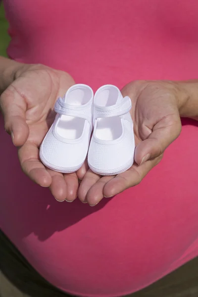 Mains avec des bottines blanches sur le ventre rose — Photo