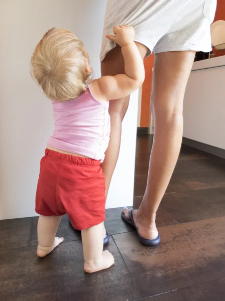 Bebê vermelho shorts agarrar mãe perna na cozinha — Fotografia de Stock