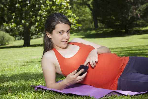 Lying pregnant with mobile looking at camera — Stock Photo, Image