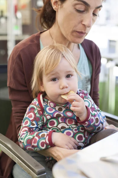 Bebê comer batatas fritas na mãe pernas — Fotografia de Stock