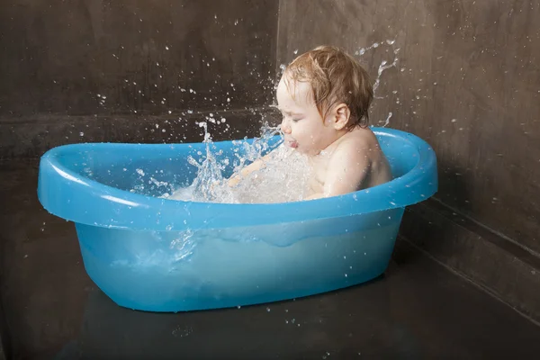 Blonde baby splashing in blue little bath indoor — Stockfoto