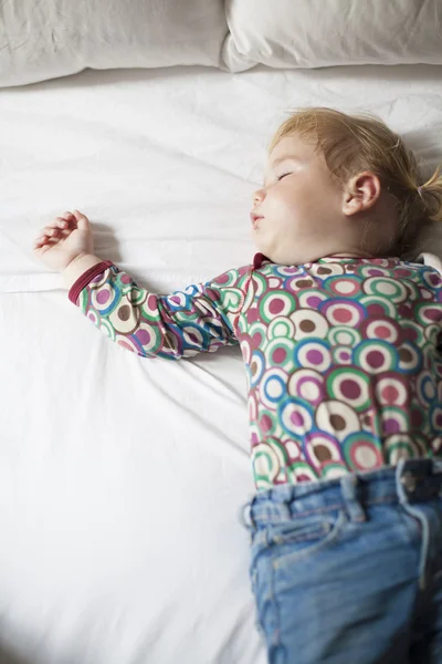 Colored shirt baby sleeping on white bed — 스톡 사진