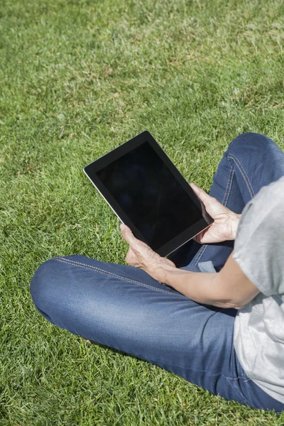 Elinde tablet çim üzerinde oturan kadın — Stok fotoğraf