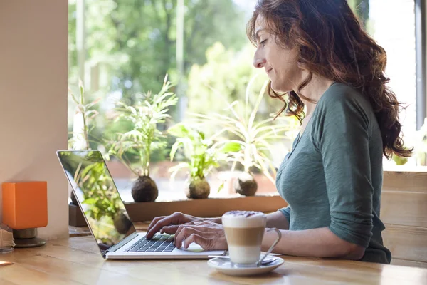 Mulher digitando laptop ao lado da janela — Fotografia de Stock