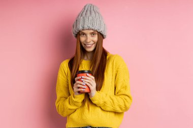 Kızıl saçlı kadın elinde tek kullanımlık kahve tutuyor.