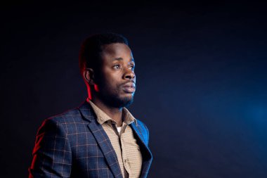 Stüdyoda karanlıkta poz veren yakışıklı adam. Sakallı, kareli takım elbiseli, siyah arka planda ciddi bir ifadeye sahip Afro-Amerikan iş adamının yakın plan portresi..