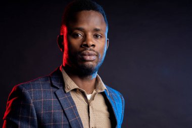 Stüdyoda karanlıkta poz veren yakışıklı adam. Sakallı, kareli takım elbiseli, siyah arka planda ciddi bir ifadeye sahip Afro-Amerikan iş adamının yakın plan portresi..
