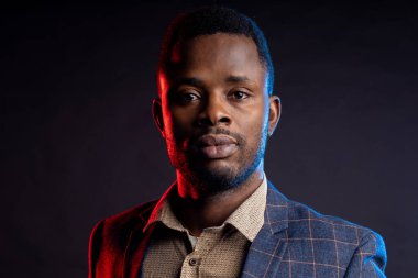 Koyu tenli, ceketli bir adam siyah arka plandaki kameraya bakar, kameraya bakar.