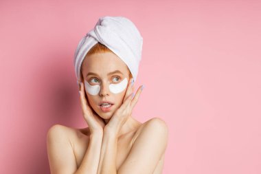 Çekici, çıplak Afrikalı bir kadın göz bantları altında koyu halkaları ve şişkinliği azaltmak için başvuruyor, avuç içlerini yanaklarında tutuyor, pembe arkaplan üzerinde duruyor ve metin için yer ayırıyor..